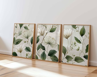 May include: Three framed floral art prints. Each print features a watercolor design of white flowers, green leaves, and stems against a light beige background. The frames are a light brown color.