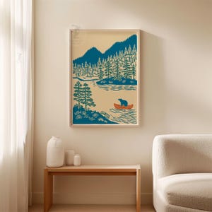 May include: A framed art print featuring a serene landscape with a teal bear in an orange canoe on a lake. Teal trees and mountains are in the background, set against a cream-colored sky. The artwork is displayed on a wall.
