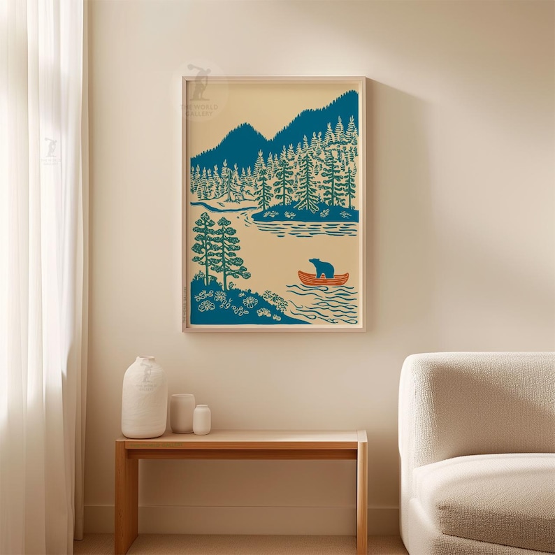 May include: A framed art print featuring a serene landscape with a teal bear in an orange canoe on a lake. Teal trees and mountains are in the background, set against a cream-colored sky. The artwork is displayed on a wall.