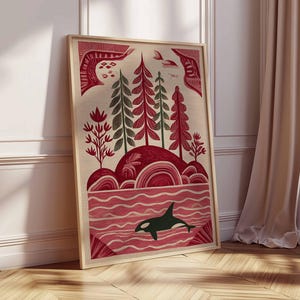 May include: Framed art print featuring a stylized landscape with red and green trees, rolling hills, and a body of water. A black and white orca swims in the water. The artwork is in a wooden frame and leans against a white wall and wooden floor.