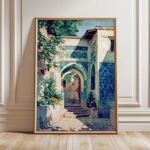 Puede incluir: Una impresión en acuarela enmarcada de un edificio arqueado con azulejos azules y blancos. La obra de arte representa un patio soleado con escaleras y vegetación. La impresión está en un marco de madera y se apoya en una pared blanca.