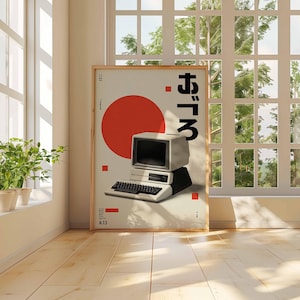 Puede incluir: Un p&oacute;ster enmarcado con un dise&ntilde;o de ordenador retro, un c&iacute;rculo rojo y texto japon&eacute;s. El ordenador es blanco y negro, con teclado y monitor. El p&oacute;ster est&aacute; apoyado en una pared cerca de una ventana.