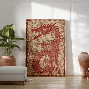 May include: A large framed artwork featuring a red dragon illustration on a beige background. The dragon is depicted with sharp teeth and claws. The artwork is displayed in a room with a plant, ottoman, and decorative vases.