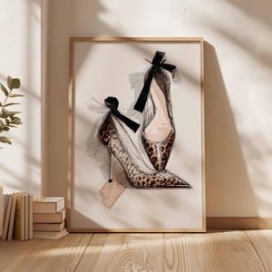 Op de afbeelding: Een ingelijste kunstafdruk van twee pumps. De schoenen hebben een luipaardprint, spitse neuzen en zwarte strikken. Het kunstwerk is gepresenteerd in een licht houten frame, geschikt voor een slaapkamer of kleedkamer.