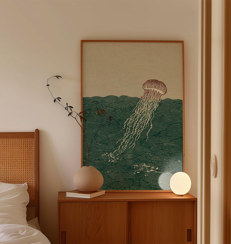May include: A framed print featuring a jellyfish in a sea of green waves. The artwork has a vintage aesthetic, with a light brown frame. A small, round, white lamp sits on a wooden cabinet below the print.