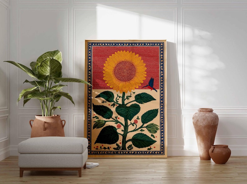 May include: A framed artwork featuring a large sunflower with a red background and a blue bird. The sunflower has yellow petals and a brown center. The artwork is displayed in a room with a plant, ottoman, and decorative vases.
