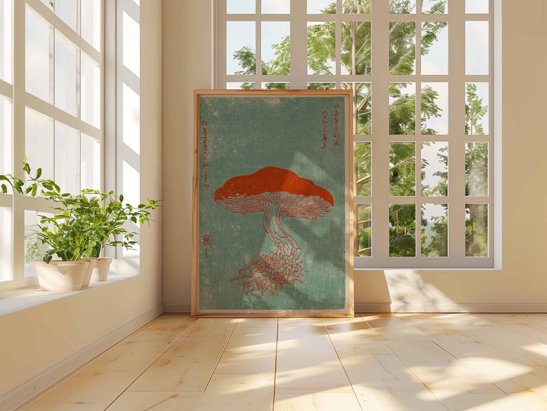 May include: A framed art print featuring a stylized orange mushroom with a detailed cap and stem against a teal background. The artwork is displayed in a bright room with a window and potted plants, creating a natural aesthetic.