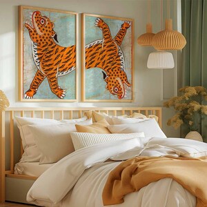 May include: Two framed prints of orange tigers on a blue background, hanging above a wooden bed frame with white bedding and a mustard yellow throw blanket.