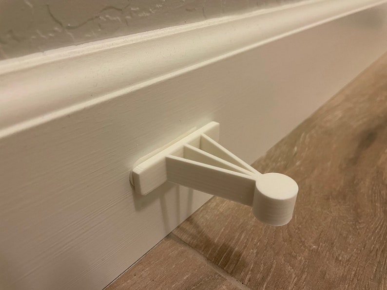 May include: White plastic door stop with a rounded end, mounted to a white baseboard.