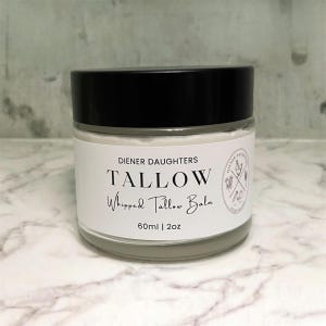May include: A white jar with a black lid containing a white cream. The label reads "Diener Daughters Tallow Whipped Tallow Balm 60ml | 2oz".