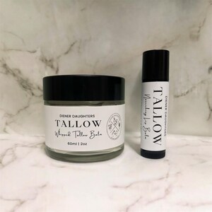 May include: Two containers of Tallow Whipped Tallow Balm by Diener Daughters. The larger container is a 2 ounce jar with a black lid. The smaller container is a lip balm stick with a black lid. Both containers have white labels with black text.