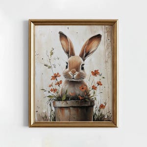 Può includere: Stampa incorniciata raffigurante un coniglio marrone con lunghe orecchie, adagiato in un vaso di terracotta con fiori arancioni e verde. L'opera d'arte ha uno stile vintage, con una cornice dorata e uno sfondo neutro.