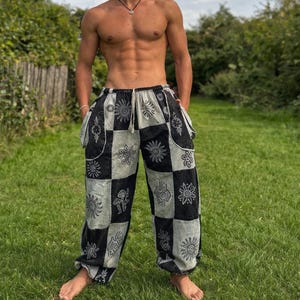 Puede incluir: Pantalones patchwork en blanco y negro con diseños de sol y flores. Los pantalones tienen cintura con cordón y bolsillos. La tela parece ligera, adecuada para climas cálidos. De estilo bohemio.