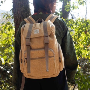 Może przedstawiać: Osoba w zielonej kurtce z beżowym plecakiem z konopi. Plecak ma klapę z zapięciem na klamrę i dwa regulowane paski. Plecak ma małą naszywkę z tekstem "Hemp & Co." z przodu.