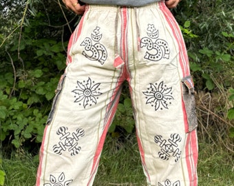Peut inclure: Pantalon blanc à rayures rouges et motifs imprimés noirs. Le pantalon a une taille à cordon et des poches cargo.