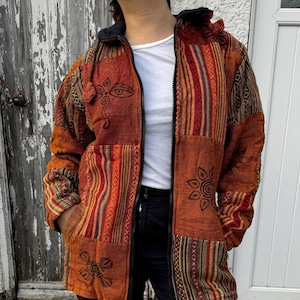 Może przedstawiać: Kurtka w stylu patchwork w wielu kolorach, zapinana na zamek błyskawiczny z kapturem. Kurtka zdobiona jest różnymi haftowanymi wzorami, w tym trzecim okiem, słońcem i mandalą.