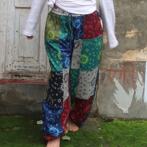 Puede incluir: Una camisa blanca de manga larga con la cintura anudada y pantalones de patchwork holgados con un patr&oacute;n multicolor de soles, lunas y estrellas en tonos azul, verde, rojo y negro con una cintura el&aacute;stica con cord&oacute;n.