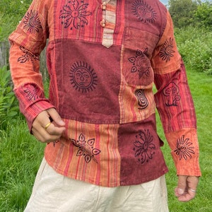 May include: A long-sleeved shirt with a patchwork design featuring various sun and flower motifs in black on a red, orange, and white striped background.