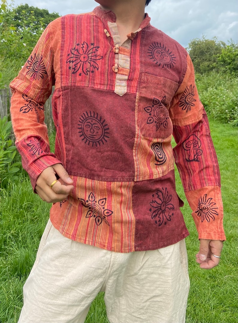 May include: A long-sleeved shirt with a patchwork design featuring various sun and flower motifs in black on a red, orange, and white striped background.