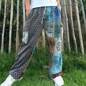 May include: Patchwork trousers with a geometric pattern and various symbols, including eyes, flowers, and mushrooms. The trousers have a drawstring waist and cargo pockets.