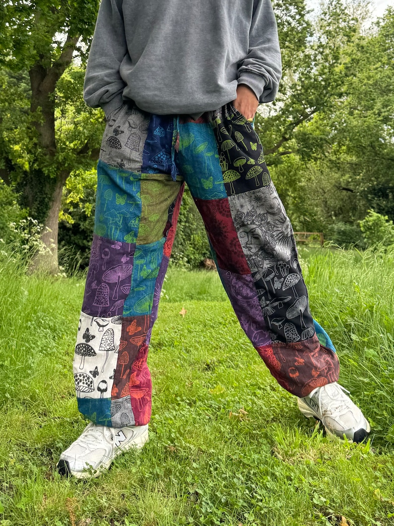 Puede incluir: Pantalones de patchwork que presentan una variedad de paneles de tela coloridos con motivos impresos de setas y mariposas. Los pantalones tienen una cintura con cord&oacute;n y se usan con una sudadera gris y zapatillas deportivas blancas.