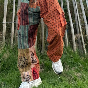 Puede incluir: Pantalón de patchwork con un patrón geométrico en naranja y negro. El pantalón tiene varios bolsillos y una cintura con cordón.