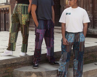 May include: Three people wearing patchwork pants. The pants are made of different colored fabrics and have a variety of patterns. The person on the left is wearing green and brown pants, the person in the middle is wearing purple and black pants, and the person on the right is wearing blue and black pants. The person on the right is wearing a white t-shirt with the letters "PZ" on the front.