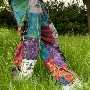 Puede incluir: Pantalones de patchwork con un dise&ntilde;o multicolor de varios cuadrados de tela. Los patrones incluyen setas, soles, lunas, mariposas y motivos florales en tonos azul, verde, morado, rojo, negro y blanco.