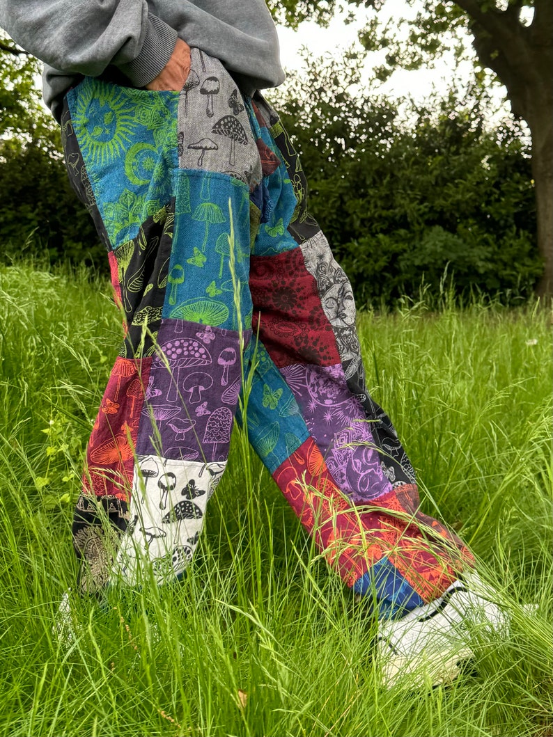 Puede incluir: Pantalones de patchwork con un dise&ntilde;o multicolor de varios cuadrados de tela. Los patrones incluyen setas, soles, lunas, mariposas y motivos florales en tonos azul, verde, morado, rojo, negro y blanco.