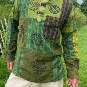 May include: A green long-sleeved shirt with a patchwork design featuring various symbols, including mushrooms, suns, and flowers. The shirt has a button-up collar and a relaxed fit.