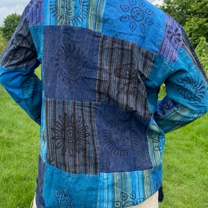 May include: A blue and black long-sleeved shirt with a patchwork design featuring sun and flower motifs. The shirt is made of cotton and has a relaxed fit.