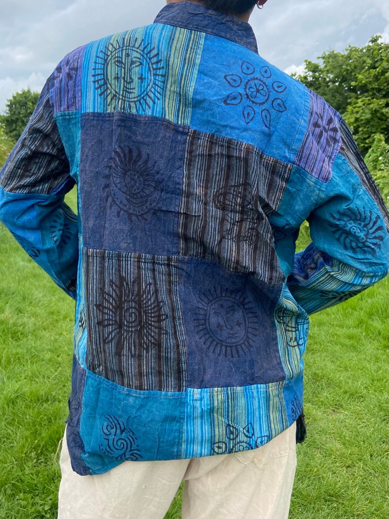 May include: A blue and black long-sleeved shirt with a patchwork design featuring sun and flower motifs. The shirt is made of cotton and has a relaxed fit.