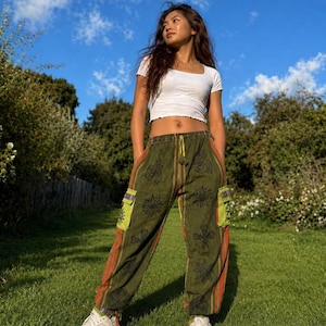 Könnte beinhalten: Ein weißes, kurzärmeliges Crop-Top kombiniert mit olivgrünen Cargohosen. Die Hose hat orange und schwarze Streifen, florale Muster und limettengrüne Taschen. Die Person trägt weiße Turnschuhe und steht auf grünem Gras.