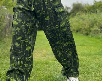 May include: Green cargo pants with a mushroom and butterfly print. The pants have multiple pockets and a drawstring waist.