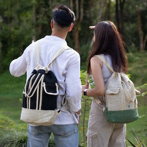 Könnte beinhalten: Zwei Personen tragen Rucksäcke aus natürlichen Materialien. Die Rucksäcke sind beide schwarz und weiß mit einem Kordelzug. Die Person links trägt ein weißes Hemd und Jeans. Die Person rechts trägt ein hellbraunes Hemd und eine Hose.