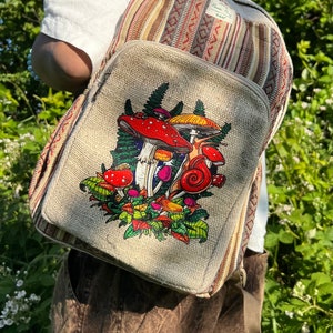 May include: A beige canvas backpack with a colourful striped pattern and a mushroom graphic. The backpack has a zipper closure and adjustable straps. The text "Home Hut" is printed on the front of the backpack.
