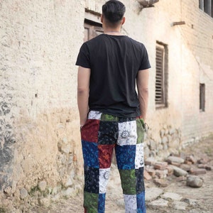 Puede incluir: Una camiseta negra de manga corta combinada con pantalones de patchwork con un patr&oacute;n multicolor de soles, lunas y estrellas en tonos rojo, azul, verde, blanco y negro. Los pantalones tienen un corte relajado y pu&ntilde;os en los tobillos.