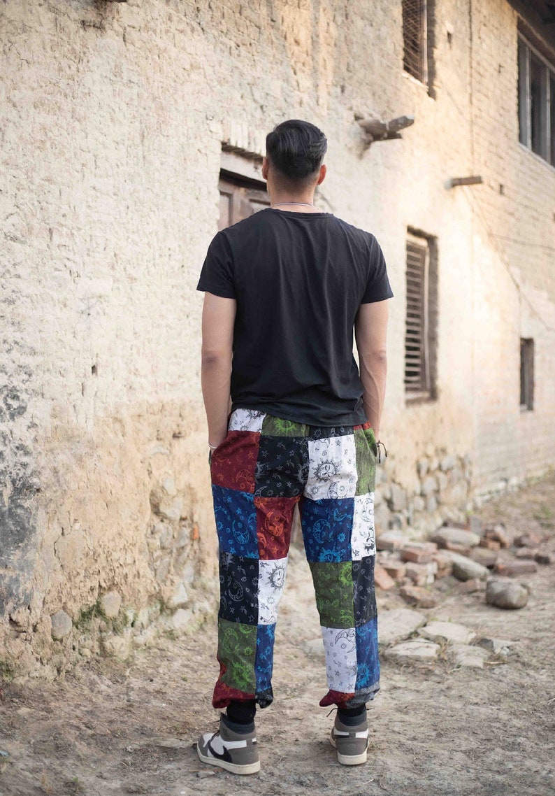 Puede incluir: Una camiseta negra de manga corta combinada con pantalones de patchwork con un patr&oacute;n multicolor de soles, lunas y estrellas en tonos rojo, azul, verde, blanco y negro. Los pantalones tienen un corte relajado y pu&ntilde;os en los tobillos.