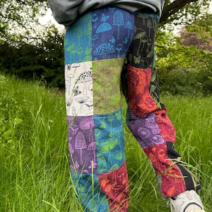 Puede incluir: Pantalones de patchwork con un dise&ntilde;o multicolor que presenta varios patrones de setas y mariposas. Los paneles de tela incluyen tonos de azul, verde, blanco, morado, rojo y negro, cosidos para formar una prenda de pantal&oacute;n largo.