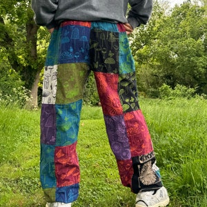 Puede incluir: Pantalones de patchwork con un dise&ntilde;o multicolor y varios estampados de setas y mariposas. Los pantalones est&aacute;n confeccionados con paneles de tela rectangulares en tonos azul, verde, rojo, morado y negro, con un patr&oacute;n repetitivo.
