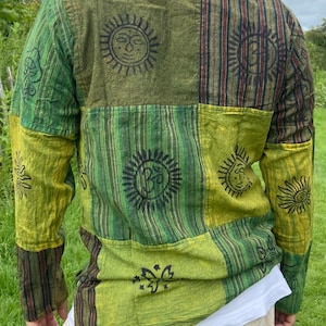 May include: A green and brown long-sleeved shirt with a patchwork design. The shirt features various sun and butterfly motifs.