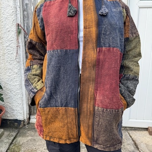 May include: A patchwork hooded jacket with a zip fastening. The jacket is made from different coloured fabrics, including red, brown, green, and blue. The jacket has a drawstring hood and two pockets.