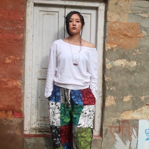 Puede incluir: Una camiseta blanca de manga larga con escote ancho combinada con pantalones de patchwork holgados que presentan un patr&oacute;n repetitivo de varios hongos y mariposas en tonos verde, rojo, azul, negro y blanco.
