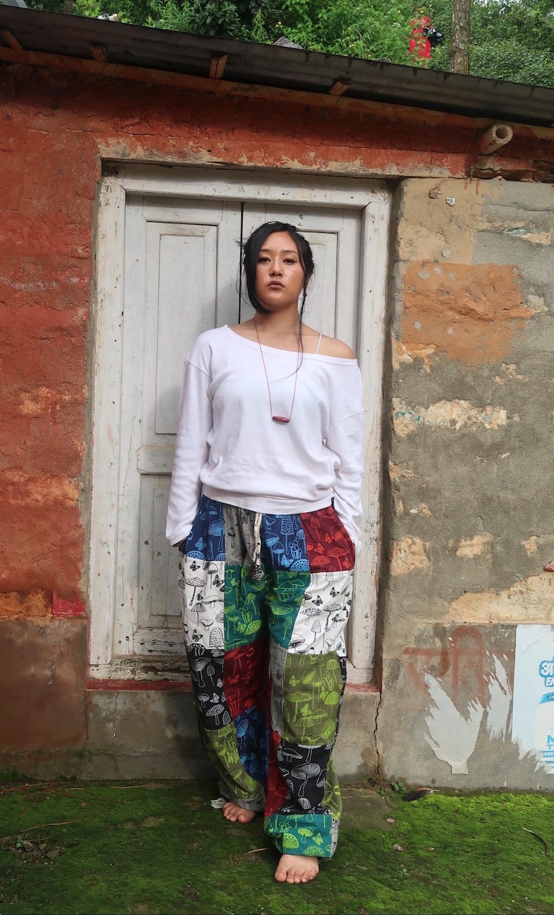 Puede incluir: Una camiseta blanca de manga larga con escote ancho combinada con pantalones de patchwork holgados que presentan un patr&oacute;n repetitivo de varios hongos y mariposas en tonos verde, rojo, azul, negro y blanco.