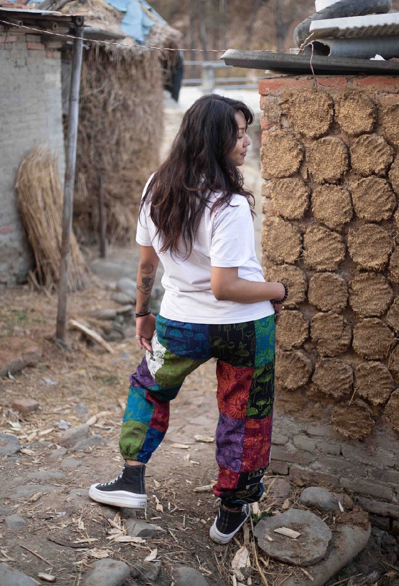 Puede incluir: Una camiseta blanca de manga corta combinada con pantalones de patchwork holgados con un estampado multicolor de setas y soles. Los pantalones tienen pu&ntilde;os el&aacute;sticos en los tobillos y se llevan con zapatillas altas de color negro y blanco.