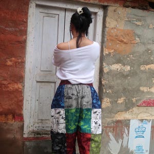 Puede incluir: Una camisa blanca de manga larga combinada con pantalones holgados de estilo patchwork con un patr&oacute;n de cuadr&iacute;cula multicolor. Cada cuadrado muestra un estampado repetitivo de setas y mariposas en tonos azul, verde, rojo y blanco.