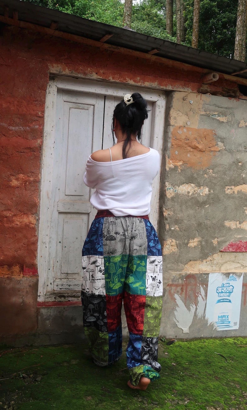 Puede incluir: Una camisa blanca de manga larga combinada con pantalones holgados de estilo patchwork con un patr&oacute;n de cuadr&iacute;cula multicolor. Cada cuadrado muestra un estampado repetitivo de setas y mariposas en tonos azul, verde, rojo y blanco.