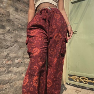 Puede incluir: Pantalón rojo de pierna ancha con estampado de sol y luna. El pantalón tiene cintura con cordón y bolsillos cargo.