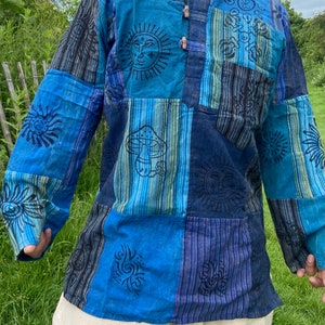 以下が含まれることがあります： 太陽、キノコ、渦巻きなどのさまざまなプリントデザインが施された、青と黒のパッチワークの長袖シャツです。