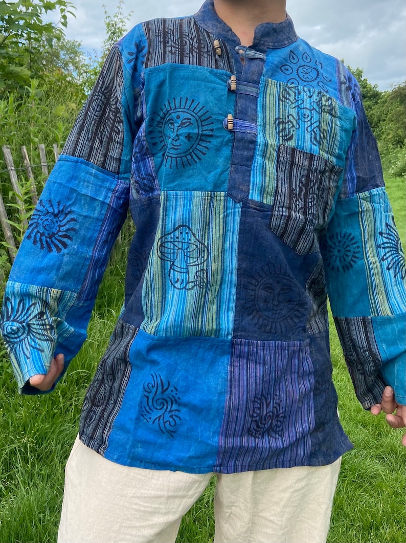 May include: A blue and black patchwork long-sleeved shirt with various printed designs, including suns, mushrooms, and swirls.